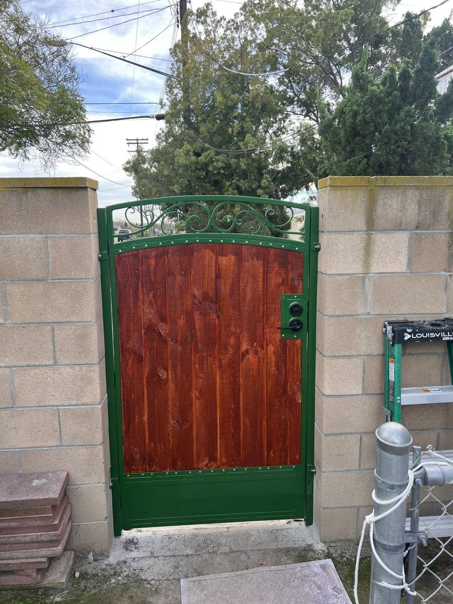 Green iron gate with stained wood panels and scroll top